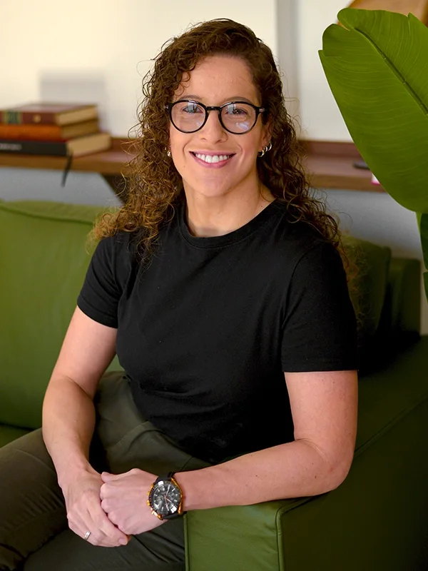 Dra. Nathalia Julio sentada em um sofá verde, em ambiente claro e acolhedor